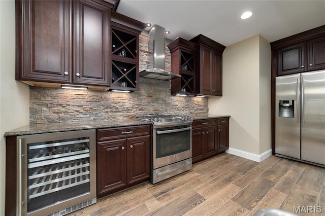 204 Logans Ct, Foristell, MO 63348 - kitchen featuring stainless steel appliances, beverage cooler, wall chimney range hood, light wood-style floors, and decorative backsplash