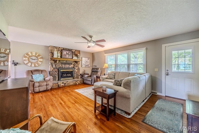 16930 Grace Rd, Lebanon, MO 65536 - living room featuring healthy amount of natural light, wood finished floors, a textured ceiling, a stone fireplace, and a ceiling fan