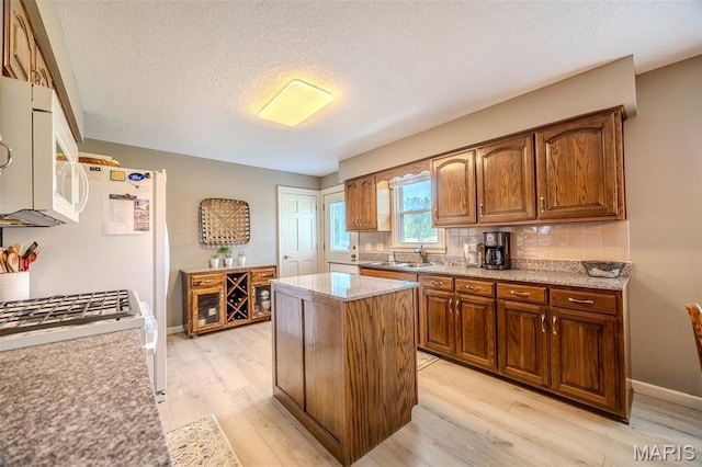 16930 Grace Rd, Lebanon, MO 65536 - kitchen featuring white microwave, light wood-type flooring, a kitchen island, a textured ceiling, and backsplash