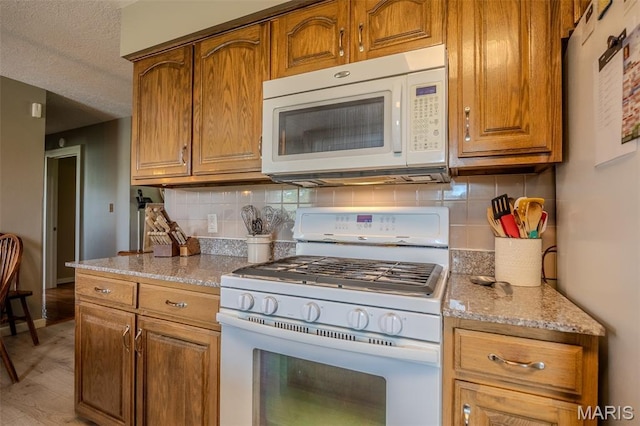 16930 Grace Rd, Lebanon, MO 65536 - kitchen featuring white appliances, backsplash, brown cabinetry, light stone countertops, and a textured ceiling