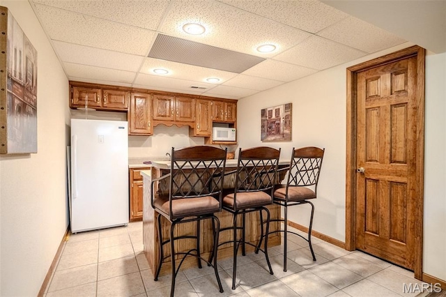 16930 Grace Rd, Lebanon, MO 65536 - kitchen with white appliances, a breakfast bar, a paneled ceiling, light countertops, and brown cabinets