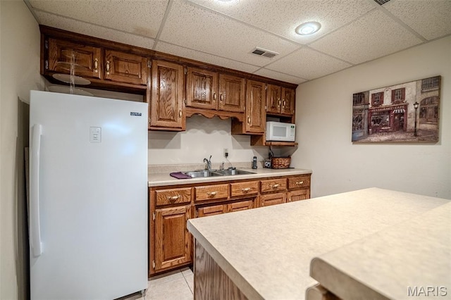 16930 Grace Rd, Lebanon, MO 65536 - kitchen featuring white appliances, light countertops, a drop ceiling, light tile patterned flooring, and brown cabinetry