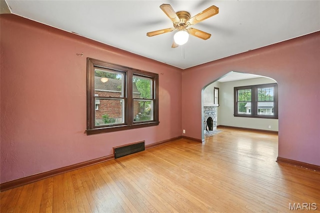 8609 Engler Ave, Saint Louis, MO 63114 - unfurnished living room with arched walkways, light wood-style flooring, ceiling fan, and a stone fireplace