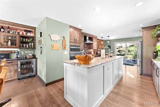 727 Madison Vly, Wildwood, MO 63005 - kitchen featuring wine cooler, appliances with stainless steel finishes, a center island with sink, light stone counters, and light wood finished floors