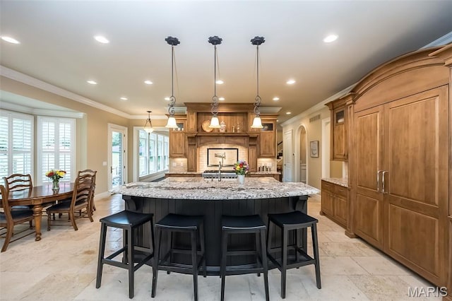 21 Lynnbrook Rd, Saint Louis, MO 63131 - kitchen featuring crown molding, a kitchen island with sink, arched walkways, light stone countertops, and recessed lighting