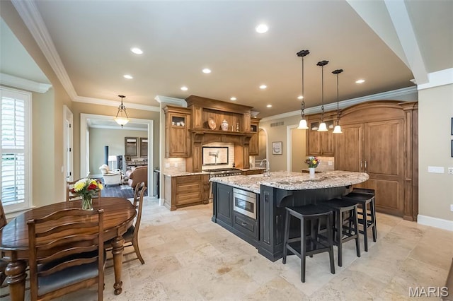 21 Lynnbrook Rd, Saint Louis, MO 63131 - kitchen featuring brown cabinets, stainless steel microwave, a large island with sink, decorative backsplash, and crown molding