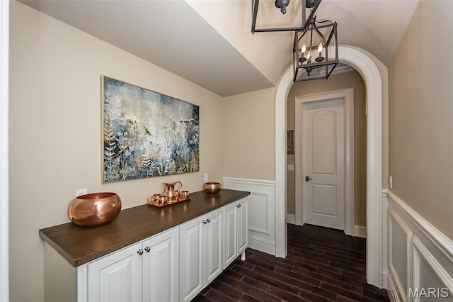 21 Lynnbrook Rd, Saint Louis, MO 63131 - corridor featuring dark wood-type flooring, arched walkways, a chandelier, a wainscoted wall, and a decorative wall
