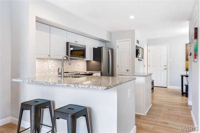 1905 King Arthur Ct, Maryland Heights Township, MO 63146 - kitchen featuring stainless steel appliances, a peninsula, backsplash, light stone countertops, and light wood finished floors