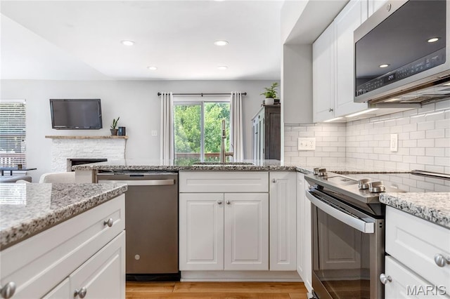 1905 King Arthur Ct, Maryland Heights Township, MO 63146 - kitchen with appliances with stainless steel finishes, a stone fireplace, decorative backsplash, white cabinetry, and light stone countertops