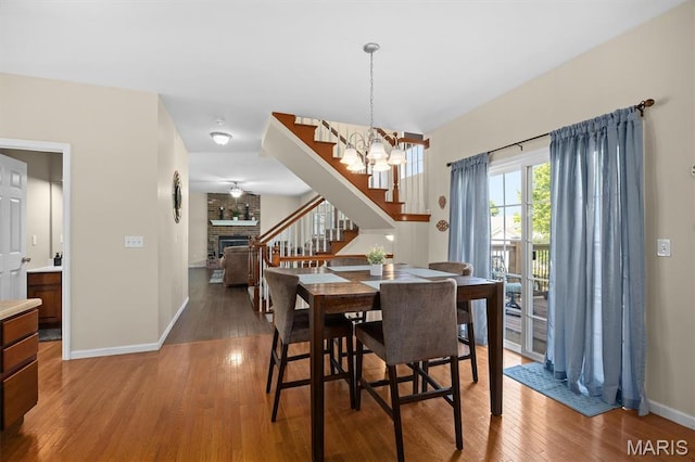 6817 Dunhill Dr, Fairview Heights, IL 62208 - dining area featuring stairway, a brick fireplace, light wood-type flooring, and a chandelier