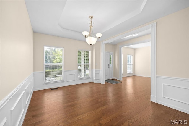6817 Dunhill Dr, Fairview Heights, IL 62208 - unfurnished dining area with wainscoting, a raised ceiling, healthy amount of natural light, a decorative wall, and dark wood-style floors