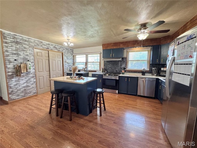 56319 Meyer Trl, Hannibal, MO 63401 - kitchen featuring appliances with stainless steel finishes, blue cabinets, a kitchen bar, light wood-type flooring, and a textured ceiling