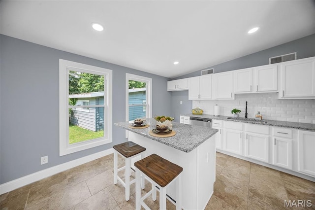 6822 Friarwood Dr, Saint Louis, MO 63134 - kitchen featuring light stone counters, white cabinetry, tasteful backsplash, stainless steel dishwasher, and vaulted ceiling