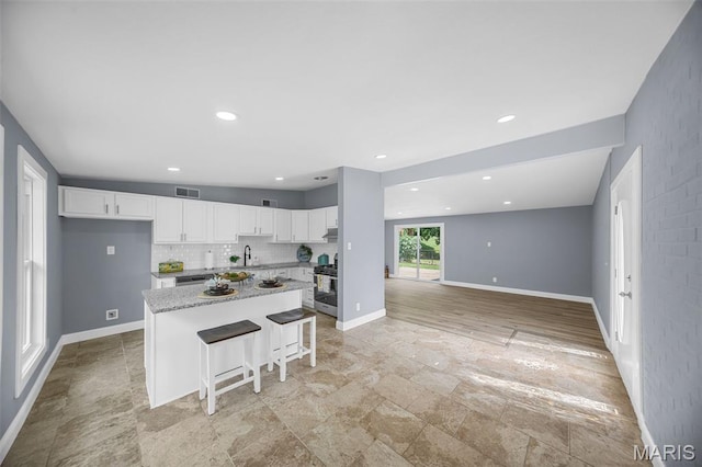 6822 Friarwood Dr, Saint Louis, MO 63134 - kitchen featuring white cabinets, a kitchen island, light stone finish flooring, a breakfast bar, and recessed lighting