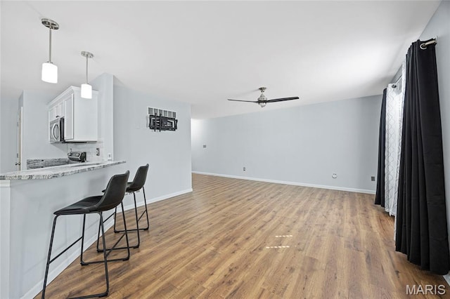 3112 Bentwater Pl, Saint Charles, MO 63301 - kitchen featuring stainless steel microwave, white cabinetry, a ceiling fan, light wood-style floors, and a breakfast bar