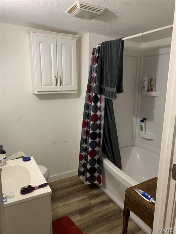 823 W Washington St, St James, MO 65559 - bathroom featuring a textured ceiling, wood finished floors, shower / bath combination with curtain, and vanity