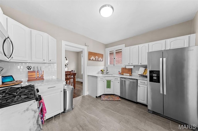 6016 Scanlan Ave, Saint Louis, MO 63139 - kitchen featuring appliances with stainless steel finishes, decorative backsplash, white cabinets, and light stone countertops