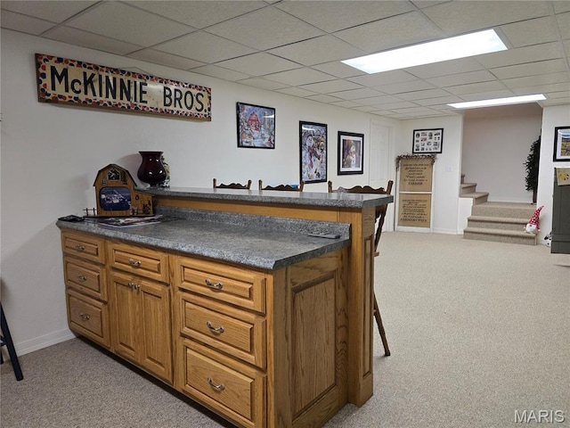 310 E 1st St, Ramsey, IL 62080 - kitchen featuring light colored carpet, a peninsula, brown cabinets, dark countertops, and a paneled ceiling