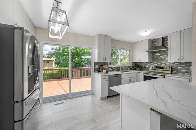 383 Messina Dr, Ballwin, MO 63021 - kitchen featuring wall chimney exhaust hood, appliances with stainless steel finishes, decorative backsplash, light stone countertops, and light wood-style flooring
