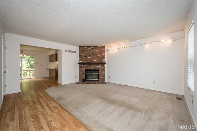 2266 Highland Hill Dr Unit F, Saint Peters, MO 63376 - unfurnished living room with a textured ceiling, wood finished floors, a brick fireplace, and a chandelier