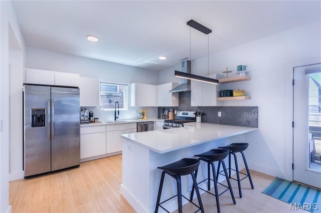 4133 Lafayette Ave, Saint Louis, MO 63110 - kitchen featuring appliances with stainless steel finishes, wall chimney range hood, a peninsula, light wood-style floors, and tasteful backsplash