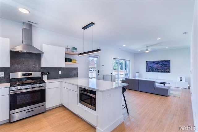 4133 Lafayette Ave, Saint Louis, MO 63110 - kitchen with stainless steel appliances, wall chimney range hood, open shelves, a peninsula, and white cabinets