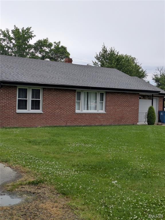 view of side of home with brick siding, a lawn, and a shingled roof