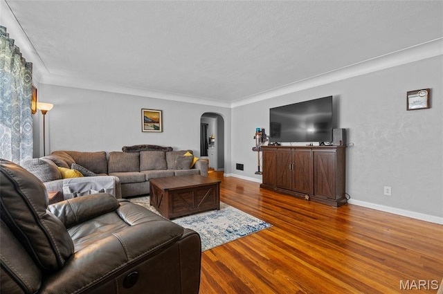 living area featuring arched walkways, wood finished floors, and crown molding