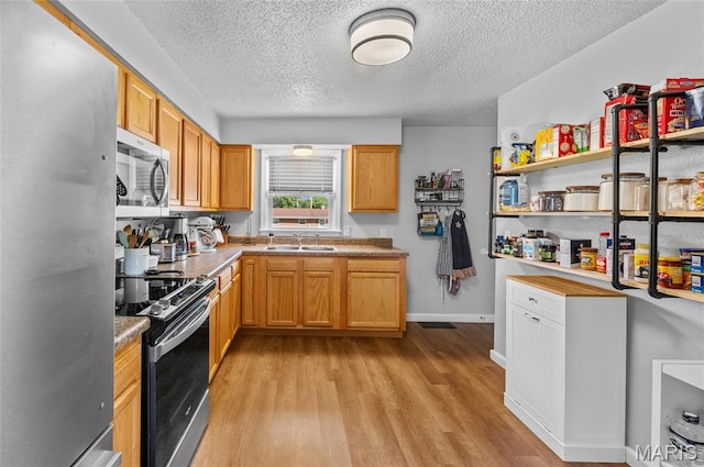 kitchen featuring appliances with stainless steel finishes, a textured ceiling, light wood-style flooring, and light countertops