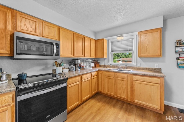 kitchen with stainless steel appliances, a textured ceiling, light wood finished floors, and light countertops