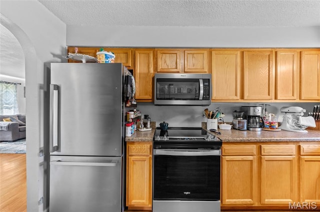 kitchen featuring appliances with stainless steel finishes, arched walkways, a textured ceiling, light wood-style flooring, and light countertops