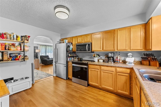 kitchen with stainless steel appliances, arched walkways, a textured ceiling, light wood finished floors, and light countertops