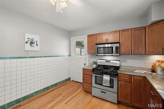 4932 Fairview Ave, Saint Louis, MO 63139 - kitchen featuring stainless steel appliances, light wood finished floors, brown cabinetry, a wainscoted wall, and ceiling fan