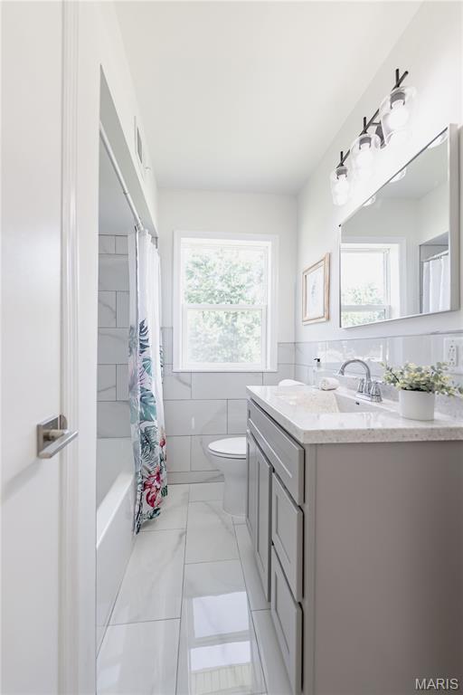7315 Cheshire Ln, Affton, MO 63123 - full bathroom with vanity, tile walls, shower / bathtub combination with curtain, marble look tiles, and wainscoting