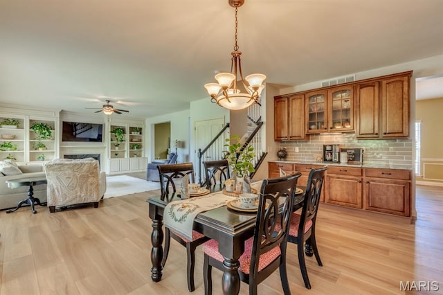 3026 Windsor Point Dr, Saint Louis, MO 63129 - dining room with light wood finished floors, a ceiling fan, a chandelier, stairs, and a fireplace