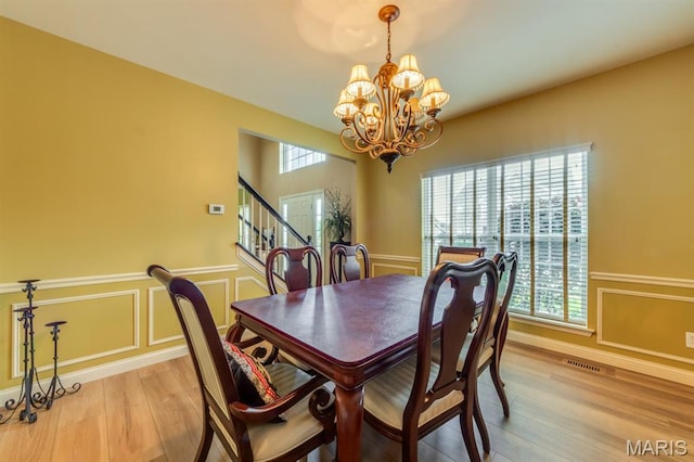 3026 Windsor Point Dr, Saint Louis, MO 63129 - dining area with a chandelier, light wood finished floors, a wainscoted wall, a decorative wall, and stairs