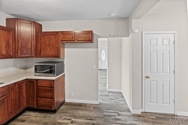 208 Washington Ave, East Alton, IL 62024 - kitchen featuring stainless steel microwave, wood finished floors, light countertops, a textured ceiling, and brown cabinets