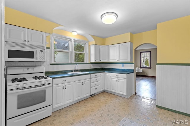 6312 Bradley Ave, Saint Louis, MO 63139 - kitchen with white appliances, white cabinets, dark countertops, arched walkways, and a wainscoted wall