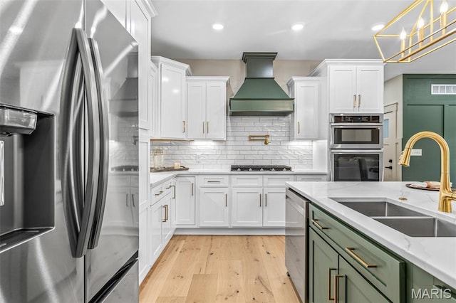10028 Debbie Pl, Bonne Terre, MO 63628 - kitchen featuring appliances with stainless steel finishes, custom exhaust hood, white cabinets, light wood finished floors, and recessed lighting