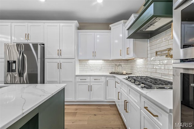 10028 Debbie Pl, Bonne Terre, MO 63628 - kitchen with stainless steel appliances, white cabinets, custom range hood, light wood-style flooring, and backsplash