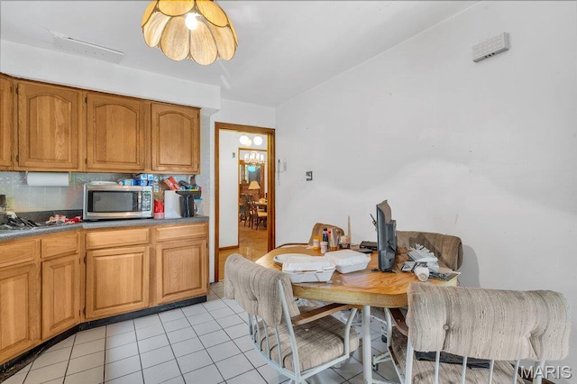 5447 Claxton Ave, Saint Louis, MO 63120 - kitchen featuring stainless steel microwave, light tile patterned flooring, tasteful backsplash, and brown cabinets