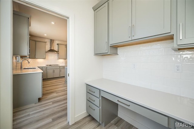 8971 Eager Rd, Richmond Heights, MO 63144 - kitchen with wall chimney exhaust hood, gray cabinetry, tasteful backsplash, built in desk, and light wood-type flooring