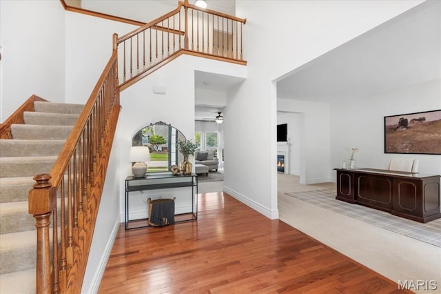 1412 Heritage Valley Dr, High Ridge, MO 63049 - staircase with wood finished floors, a ceiling fan, a glass covered fireplace, and a high ceiling
