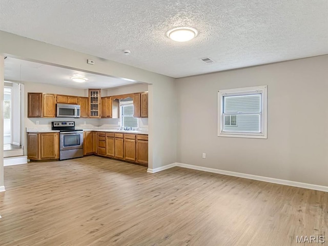 628 E Chain Of Rocks Rd, Granite City, IL 62040 - kitchen featuring appliances with stainless steel finishes, brown cabinetry, light wood-style flooring, light countertops, and glass insert cabinets