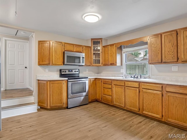 628 E Chain Of Rocks Rd, Granite City, IL 62040 - kitchen featuring appliances with stainless steel finishes, light countertops, brown cabinets, light wood-type flooring, and glass insert cabinets