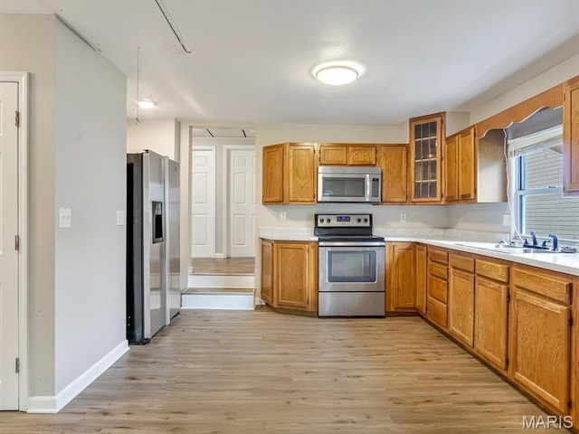628 E Chain Of Rocks Rd, Granite City, IL 62040 - kitchen with appliances with stainless steel finishes, light wood finished floors, light countertops, brown cabinets, and glass insert cabinets