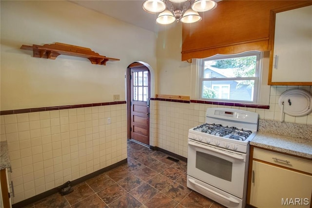 301 E 7th St, Alton, IL 62002 - kitchen with white gas range oven, tile walls, arched walkways, wainscoting, and a chandelier