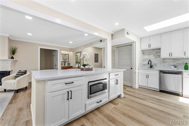 115 E Bodley Ave Unit A6, Kirkwood, MO 63122 - kitchen featuring appliances with stainless steel finishes, crown molding, a skylight, open floor plan, and light wood-type flooring