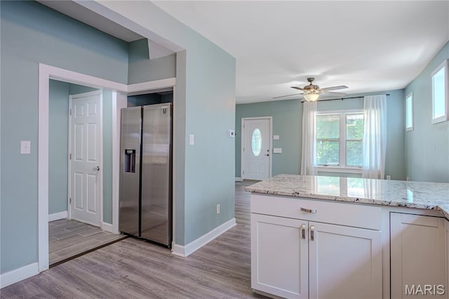 6557 Marmaduke Ave, Saint Louis, MO 63139 - kitchen with stainless steel fridge, light wood finished floors, white cabinets, and light stone counters