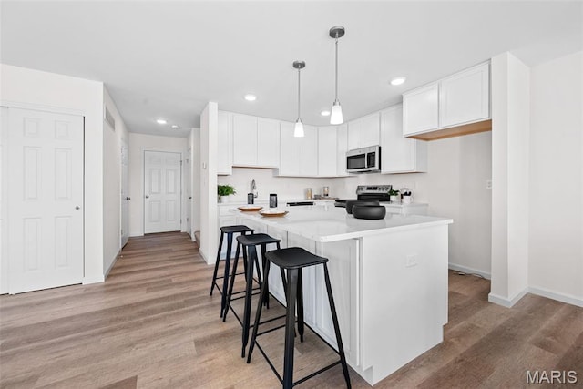 2921 Memphis St, Saint Charles, MO 63301 - kitchen with stainless steel appliances, white cabinetry, light wood-style floors, recessed lighting, and a center island
